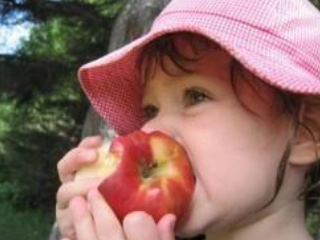 Enfant avec un chapeau rose qui croque dans une pomme. 